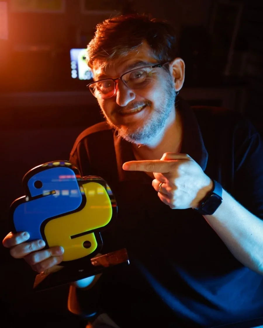 Aislan Greca segurando um troféu com o símbolo do Python, em luz azul e laranja