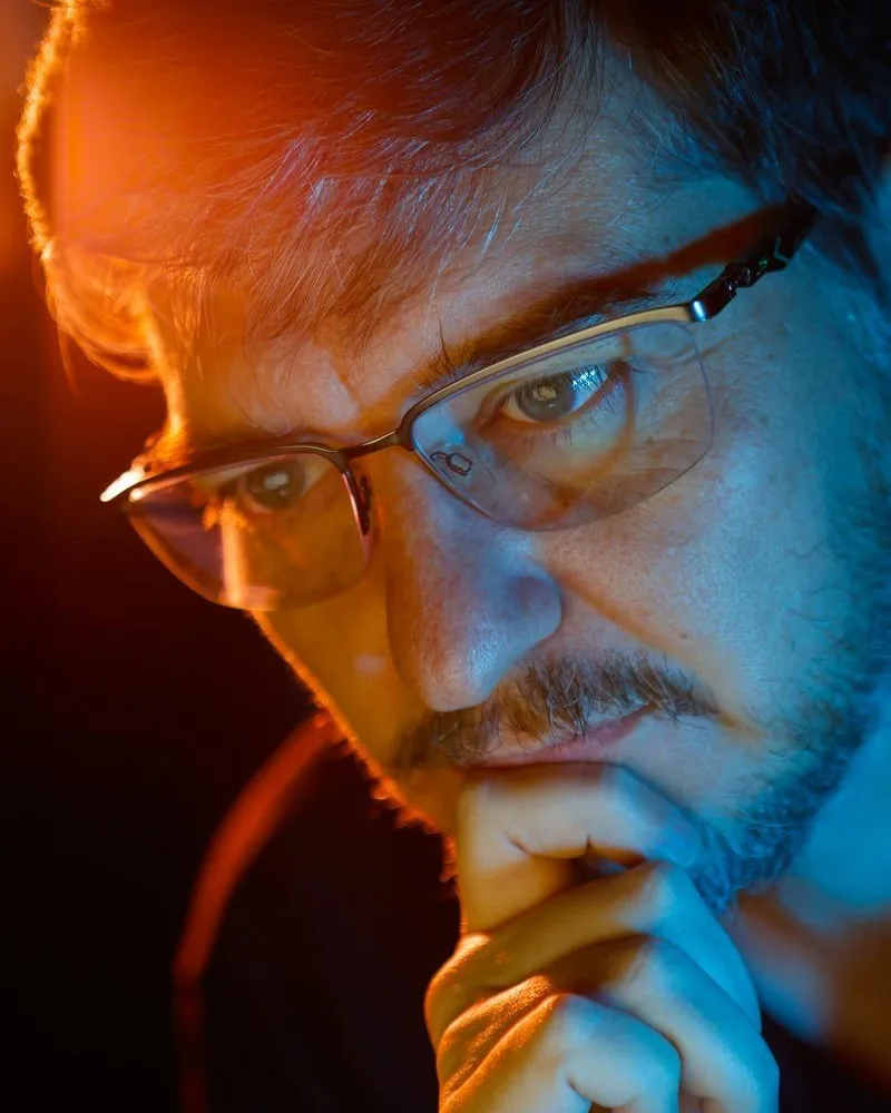 Retrato de Aislan Greca, pensativo, com a mão no queixo, em luz azul e laranja